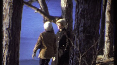 1979: two women wearing woolen caps and sweater standing amid trees on the shore