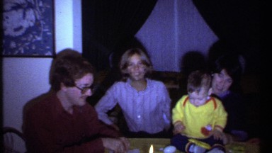 1979: baby sits on table with candles on it surrounded by parents and siblings