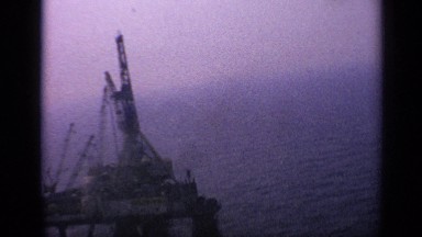 1970: a small boat moving past an oil rig in the ocean UNITED KINGDOM