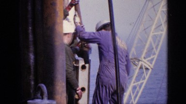 1970: a team of workers in hard hats work together on an oil rig along the ocean