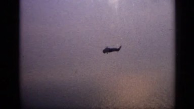 1970: Lone Helicopter Flies Over Ocean with Reflecting Rotor Blade