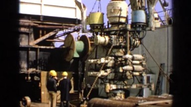 1970: Three Men in Yellow Hard Hats Standing Alongside a Large Piece