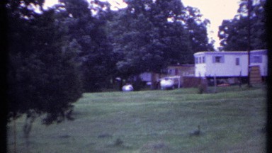 1971: rvs or trailers looking out over rolling hills and a small lake or body
