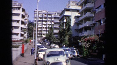 1970: woman walking down the street pass parked antique cars. INDIA
