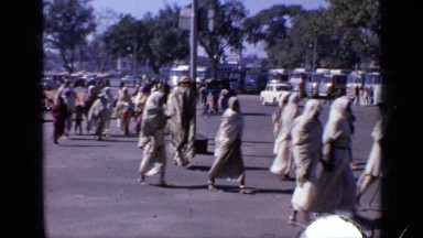 1970: a group of women with veil on head walking along the road near to a shrine