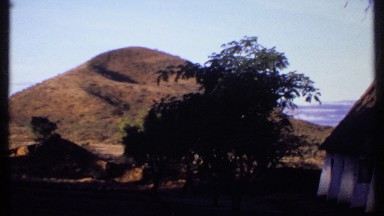 1969: man walks away from white building, under trees and toward mountain KENYA