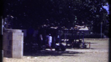 1969: yellow field with buildings and trees surrounding it and a couple people