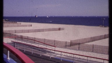1969: man strolls alone on boardwalk by beach divided by wooden fencing