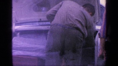 1968: two man in mechanic shop repairing and placing box in car front