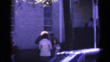 1968: people are shown standing outside on the sidewalk near a car and building