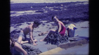 1968: family build sand castles at the beach and wave to the camera. FLORIDA