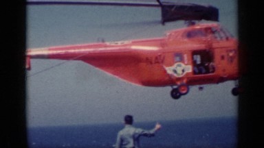 1962: a red color helicopter about to land on the runway on the shore of the sea
