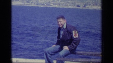 1962: A Man Sits on Forks of Large Forklift at Industrial Dock Adjacent to Bay