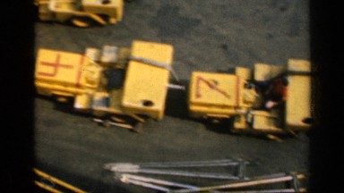 1962: construction site with parked yellow trucks and employees walking around.