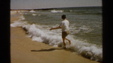 1959: a short-haired woman and a boy dressed in shorts wade in the incoming tide