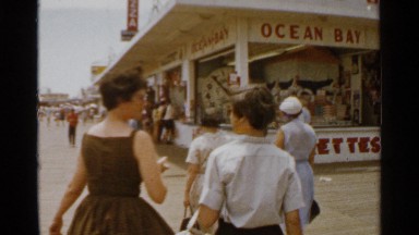 1959: two women and a boy stroll on wide boardwalk with shops on one side