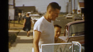 1959: man closes car door for wife then walks around car talking to camera.