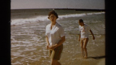 1959: mother spending time with her son playing in seashore waves during holiday