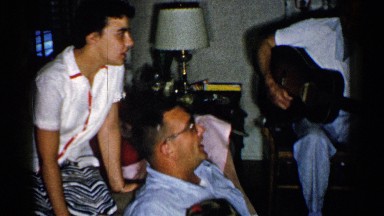 1952: family sitting in a living room singing along to man playing guitar.