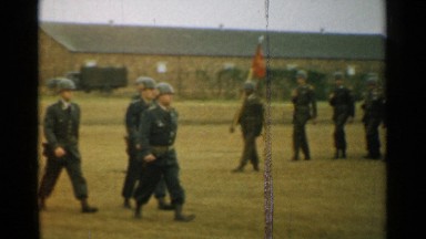 1952: a military troop is doing march past in the ground with their flag ahead