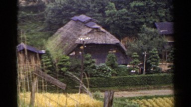 1953: road separates low buildings with wide roofs from divided farm land JAPAN