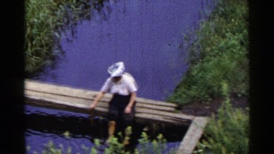 1953: a woman sitting on a bench over a water filled canal, pulling something