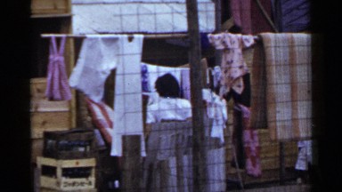 1953: woman does washing while son plays with a stick in back garden. JAPAN