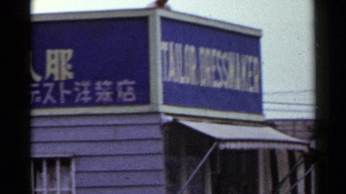 1953: various buildings on the side of a dirt road, one with foreign text