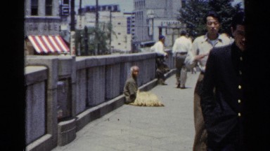 1953: beggar sits in the street as men pass by in china. JAPAN