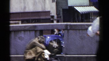 1953: A Guy in Camo Sitting Downtown with a Hole in Fence Showing Blue Painted