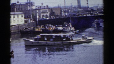 1953: camera pans on boats in a marina with a quaint town in the background.