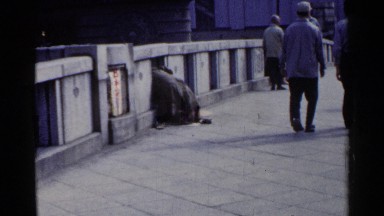 1953: a man looks between the posts of a bridge while a crowd walk past him.