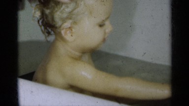 1939: Young Child Sits in Tub and Wipes Face While Hair Is Being Shampooed