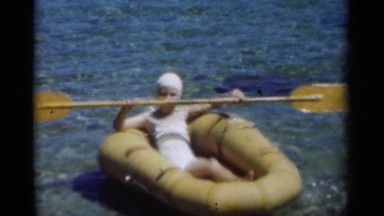 1949: girl floats inside yellow inflatable boat using double-paddled oar