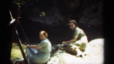 1949: two women in long dresses sit next to a creek with a rocky bank SANTA CRUZ