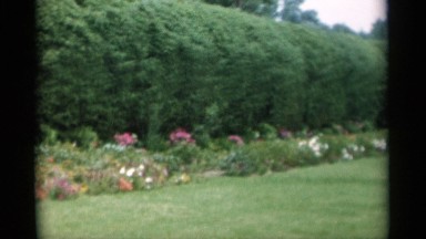 1956: tombstone outside surrounded by beautiful flowers and bushes. JONES BEACH