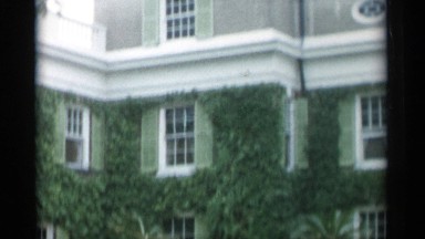 1956: large house with many people walking around and vegetation growing