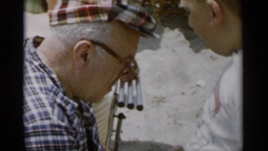 1956: grandfather in hat shares food with grandson at the beach. JONES BEACH