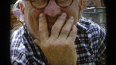 1956: an older man at a party, eating food and smiling in his hand. JONES BEACH