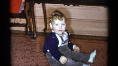 1955: young child sits on rug while older boy hides face behind lifted book