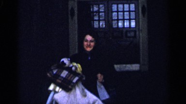 1955: woman carrying many items walks out of doorway and gives a kiss NEW YORK