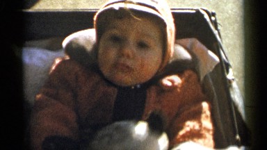 1955: a cute baby sitting at her baby chair and her mother or father putting toy