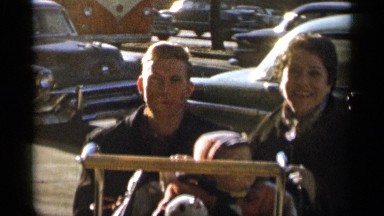 1955: smiling couple sit close together with tiny child bundled up for the cold