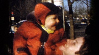 1955: happy baby getting held up, cheeks pinched, and bounced by a woman