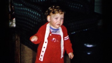 1955: young child in red coveralls smiles and toddles for the camera. NEW YORK