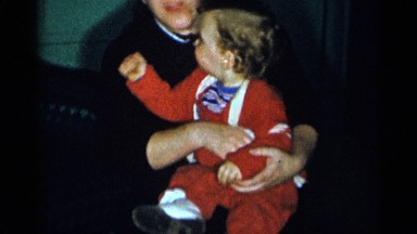 1955: funny kid wearing red dress playing in the lap of loving mother NEW YORK