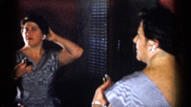 1955: an old fat woman standing in front of the mirror and staining the hair