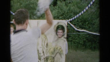 1954: a man is standing behind a funny painting and being hit by wet balls