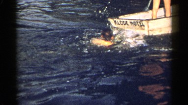 1954: boy swims to brother on a lake in a small boat. NEW YORK