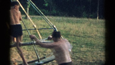 1954: men and kids are playing on a small swings a the ground morning time.